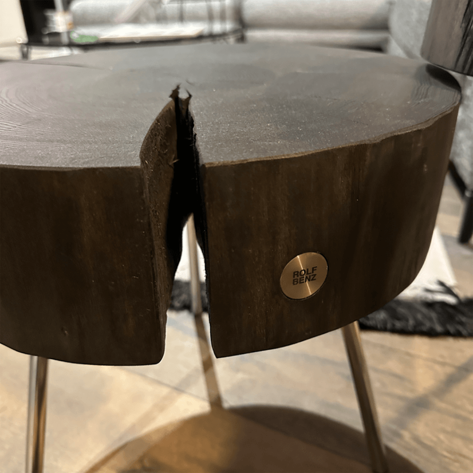 Detailaufnahme eines modernen Beistelltischs aus dunklem Holz mit einem Metalllogo von Rolf Benz, platziert auf einem stylischen Gestell.