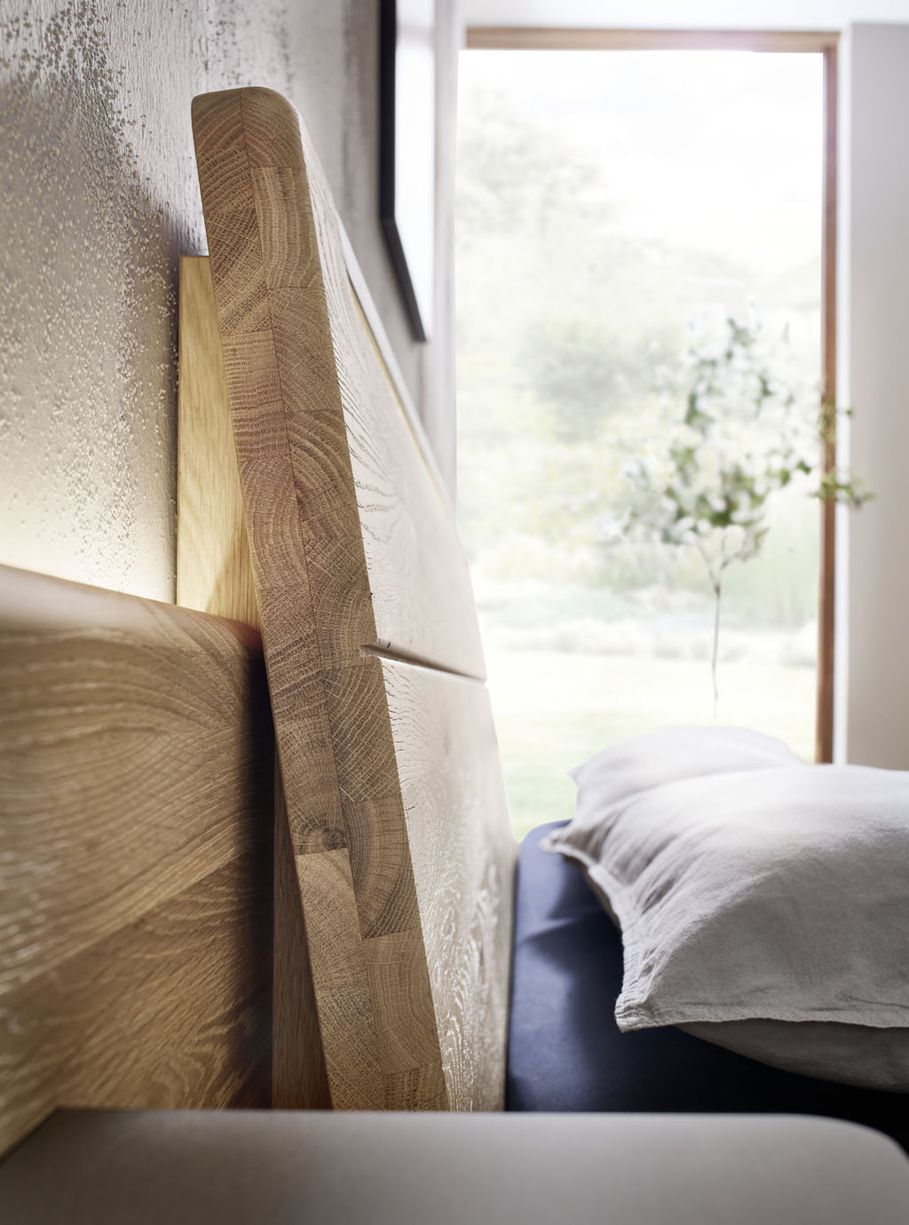 Detailaufnahme eines modernen Holzbettes mit Beleuchtung am Kopfteil stilvoll dekoriert