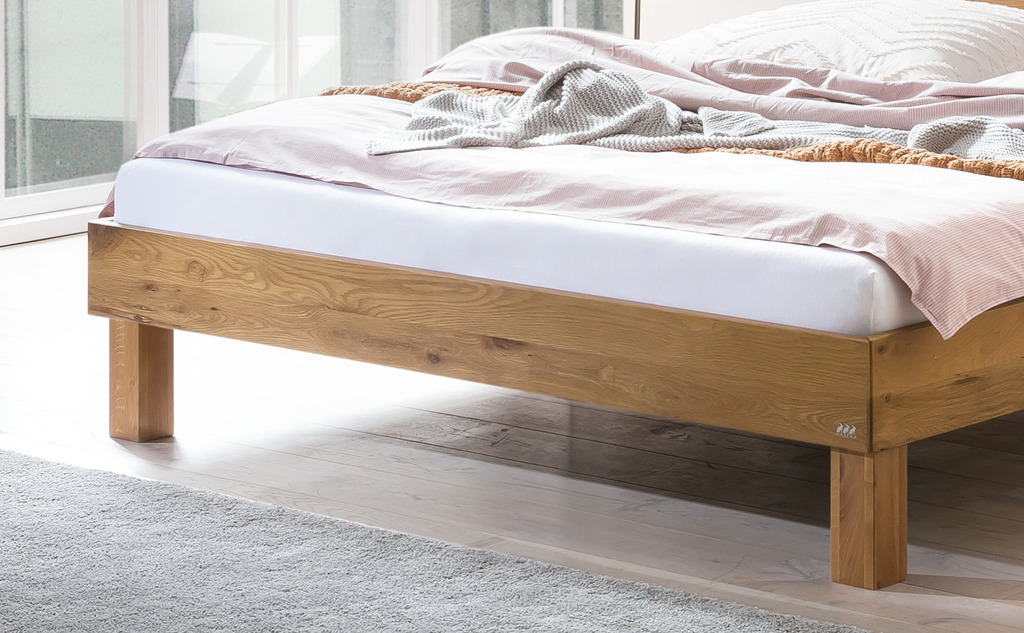 ausschnitt eines braunen Holzbettes mit einer matratze mit weißem bezug und bettschwäsche in einem modernen zimmer hasena