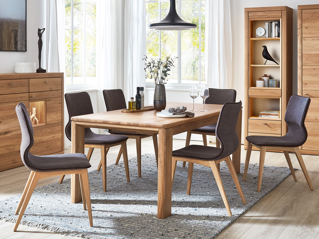 Wöstmann Aurum - Esstisch | Type 3290 | Wildeiche massiv | B: 95 cm | 4 Größen konfigurierbar Gemütliches Esszimmer mit Holztisch, sechs Stühlen und modernen Dekorationen vor großen Fenstern