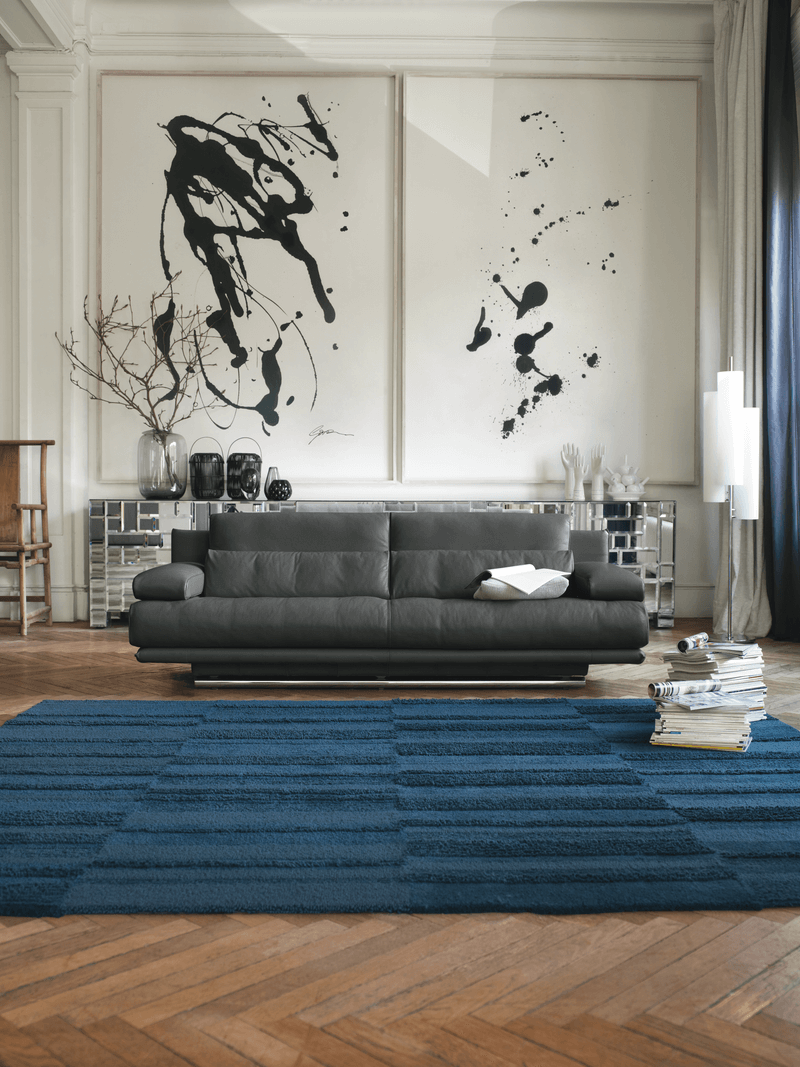 Ein modernes Wohnzimmer mit einem schwarzen Ledersofa, blauer Teppichmatte und abstrakter Kunst an der Wand