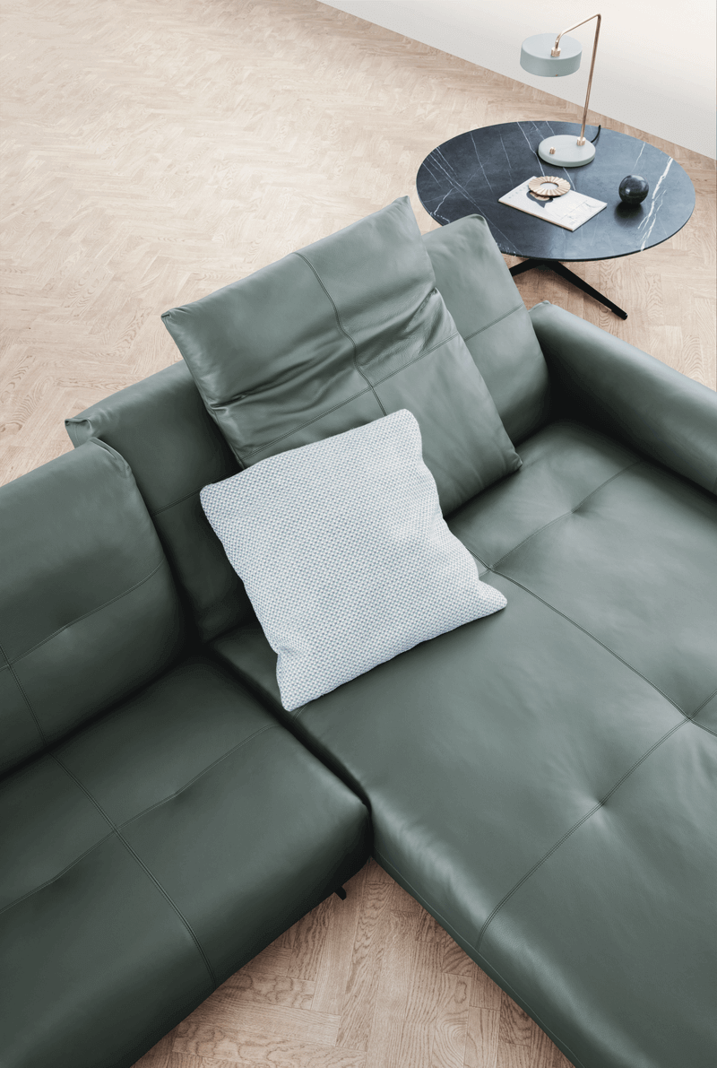 Das Bild zeigt ein modernes Ecksofa von Rolf Benz 50 in einem hellen Interieur mit einem runden Couchtisch und dekorativen Elemente.