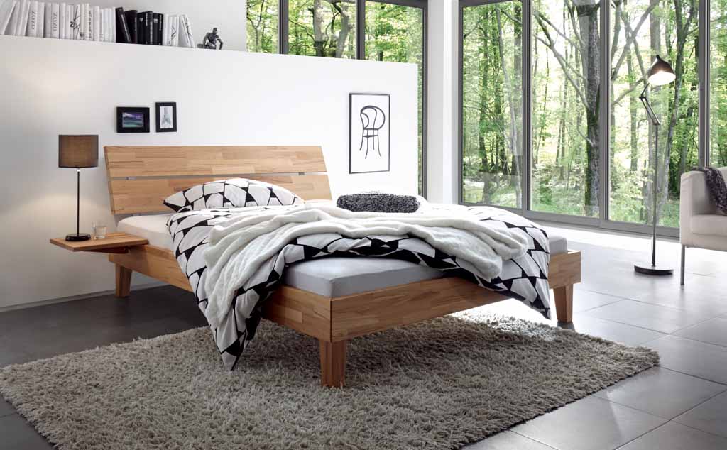 Hasena Wood-Line Bettanlage | Kernbuche natur, geölt Stilvolles Schlafzimmer mit einem Holz-Doppelbett, dekorativen Kissen und einer großen Fensterfront, die den Blick ins Freie bietet.