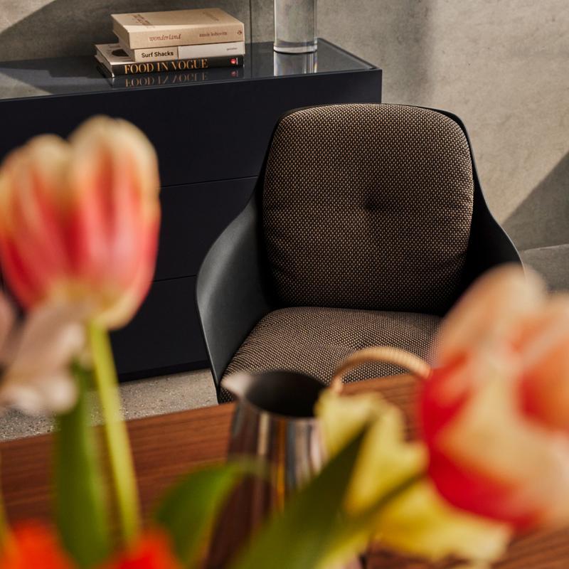 Nahaufnahme eines modernen Sessels vor einem schwarzen Möbelstück, mit Blumen im Vordergrund