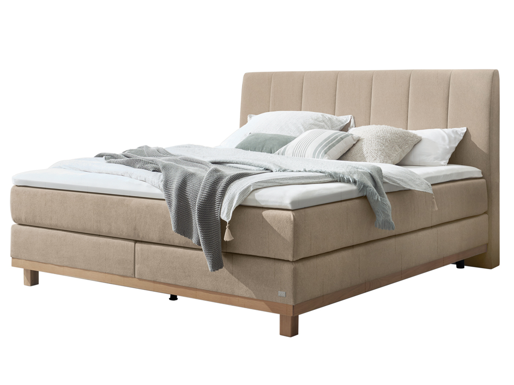 Das Boxspringbett mit beigem Kopfteil und Holzfüßen, frontal vor einem weißen Hintergrund abgebildet.