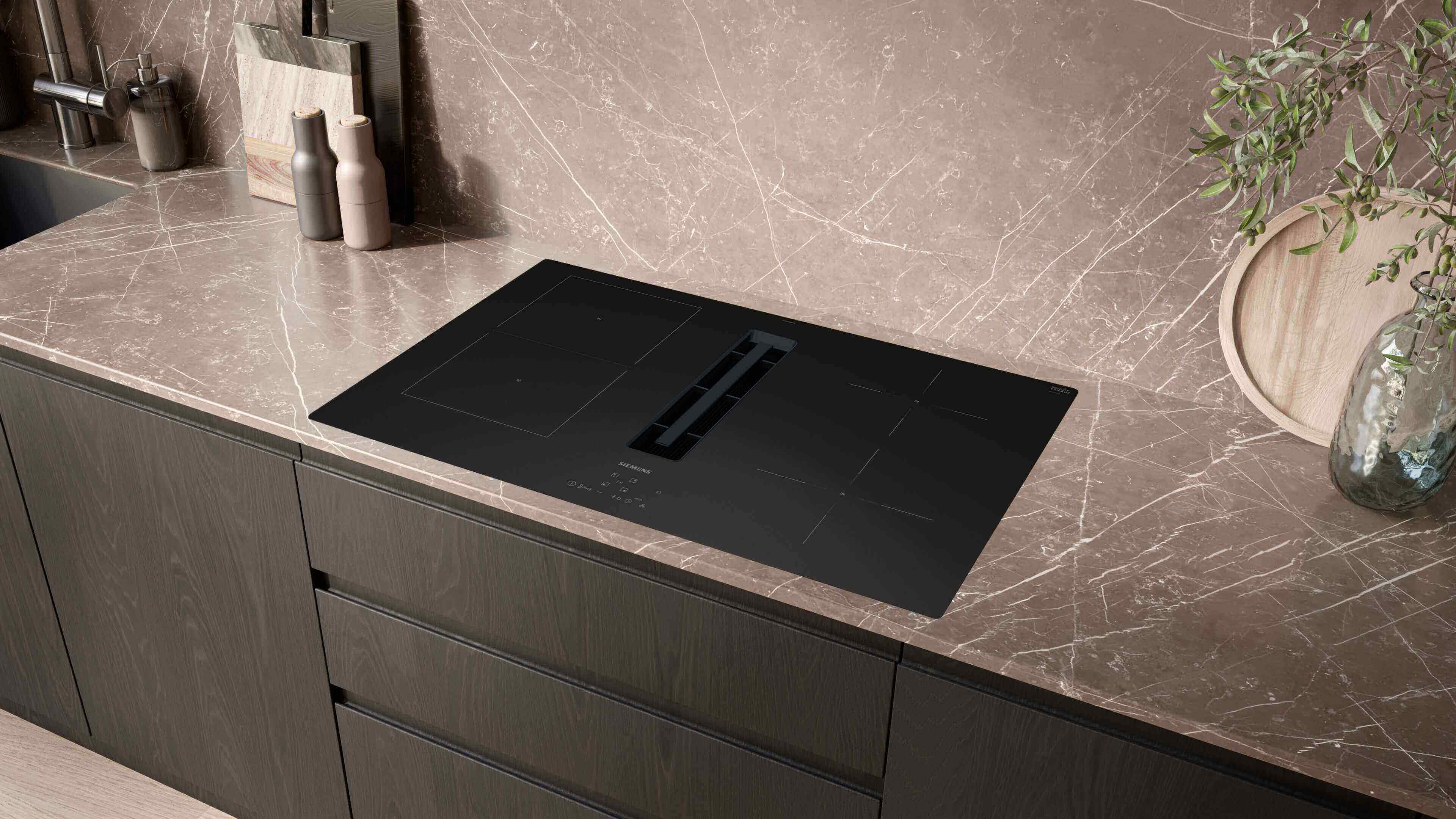 Modernes Siemens studioLine Induktionskochfeld mit integriertem Dunstabzug in eine elegante, dunkle Marmorarbeitsplatte einer Küche eingebaut.