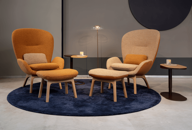 Zwei bequeme, modern designte Sessel mit passenden Fußhockern auf einem dunkelblauen Teppich, umgeben von kleinen Beistelltischen