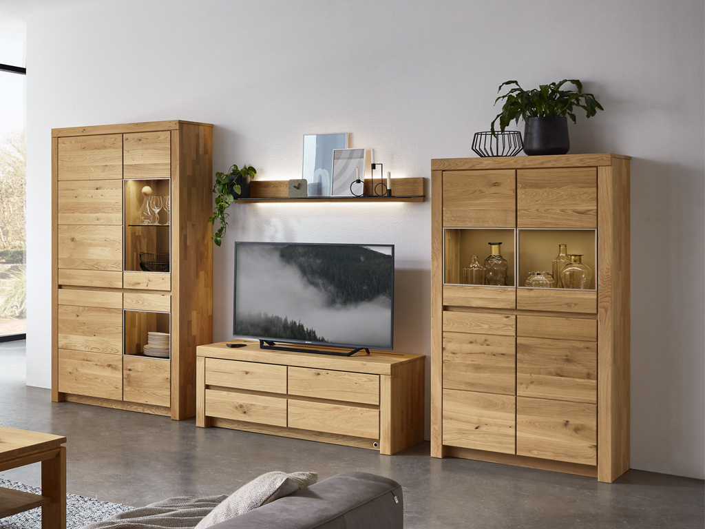 Wohnzimmer mit Holz-Schrankwand, bestehend aus TV-Schrank, Regal und Vitrinen, dekoriert mit Pflanzen und Glasobjekten