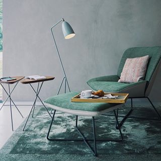 Stylisher Wohnbereich mit grünem Sessel, Beistelltischen und Stehlampe auf einem Teppich mit Tablett und Buch