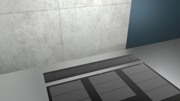 Schicke Küchenarbeitsplatte mit eingebautem Induktionskochfeld und Dunstabzug vor einer Betonwand