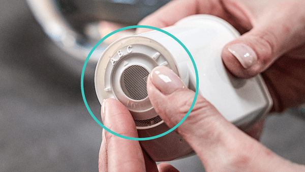Nahaufnahme von Händen, die den runden Einstellring für die Wasserhärte am unteren Ende des Kaffeemaschinen-Wasserfilters einstellen.