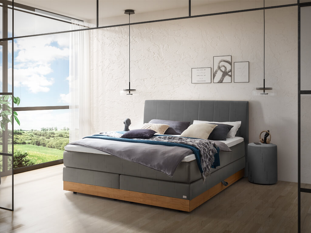 Ein stilvolles Schlafzimmer mit einem dunkelgrauen Boxspringbett mit einem eleganten Kopfteil und einem Holzbettrahmen.