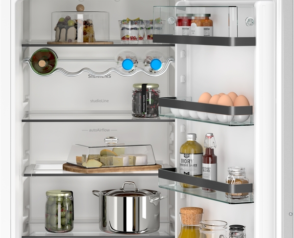 Innenansicht des Kühlschranks mit Flaschenregal, AutoAirflow-System und gut gefüllten Glasablagen, darunter Käse unter einer Haube und ein Kochtopf.