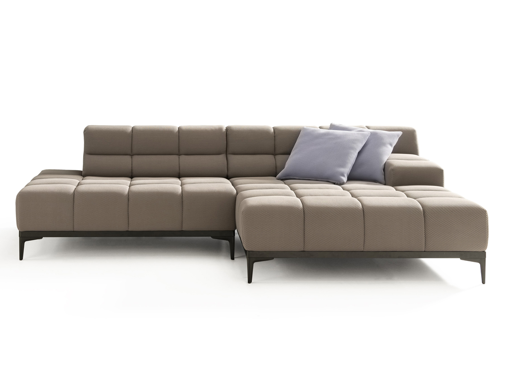 Ein L-förmiges, modulares Ecksofa in Hellbraun mit einem feinen Punktmuster und gesteppten Sitz- und Rückenkissen. Es steht auf schlanken schwarzen Metallfüßen. Zwei hellblaue Zierkissen liegen auf der Rückenlehne. Der Hintergrund ist weiß.