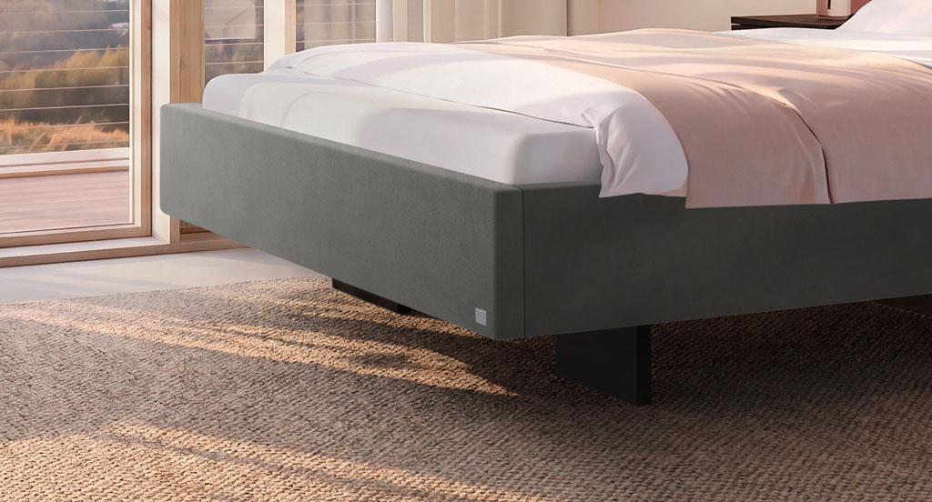 Nahaufnahme der schwarzen Füße an einem grauen Polsterbett mit Textilbezug in einem Schlafzimmer (KI-generiert)
