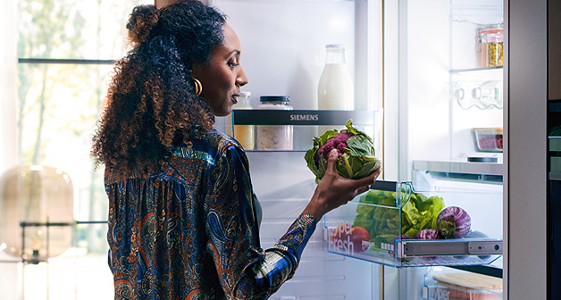 Frau steht an einem geöffneten Siemens studioLine Einbau-Kühlsrank und holt einen Kohl aus der Kühlung.