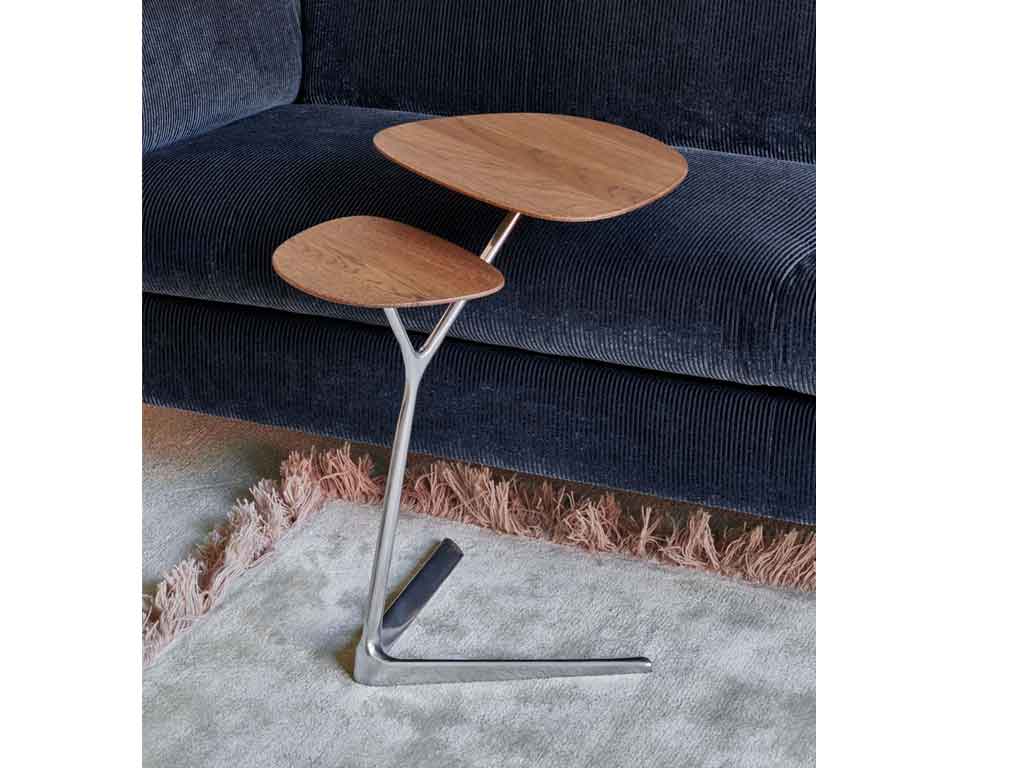 Ein eleganter, zweistufiger Beistelltisch aus Holz mit einem silbernen Metallgestell steht auf einem Teppich neben einem dunkelblauen Sofa.