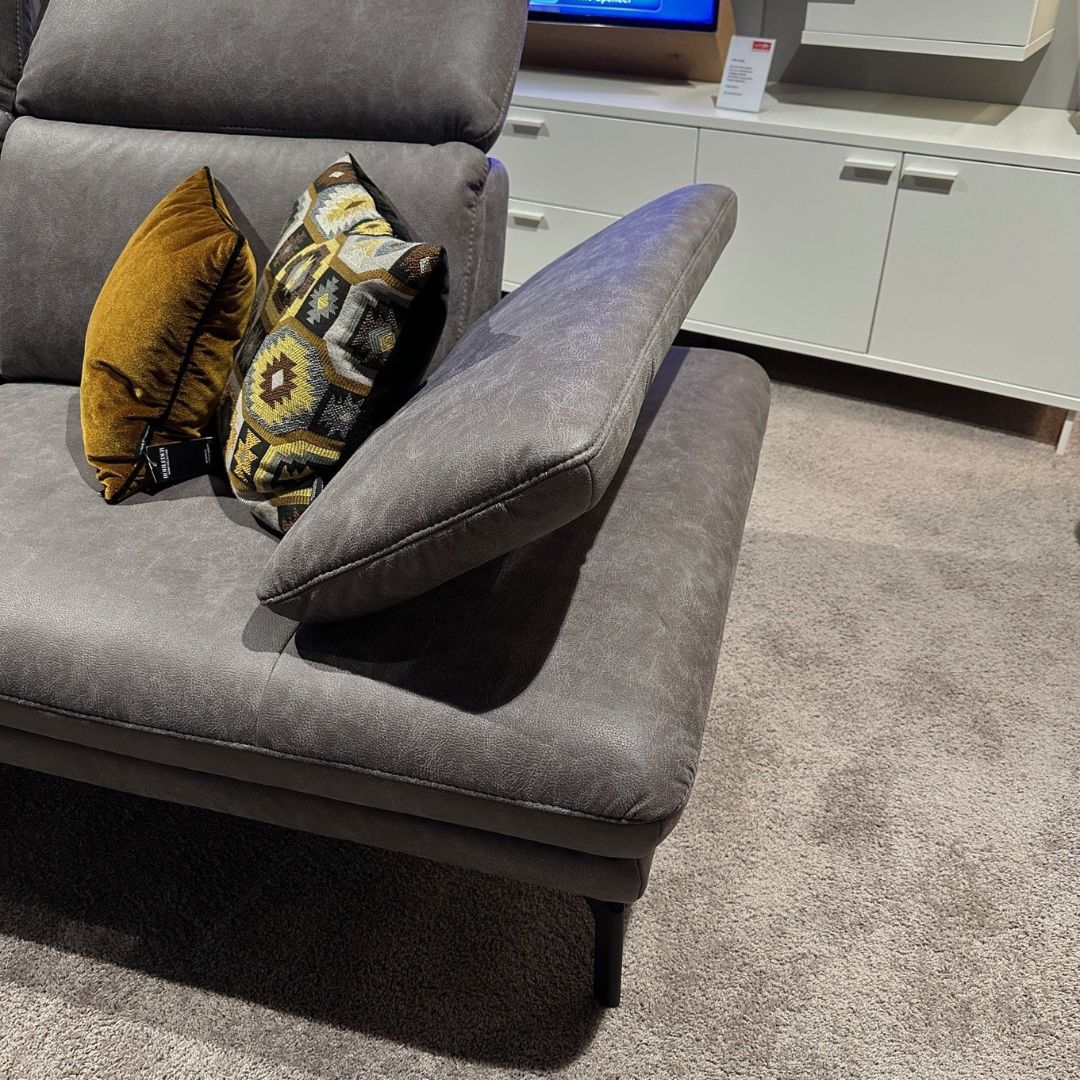 Graue Couch mit gelben und gemusterten Kissen auf Teppichboden vor einem weißen Sideboard