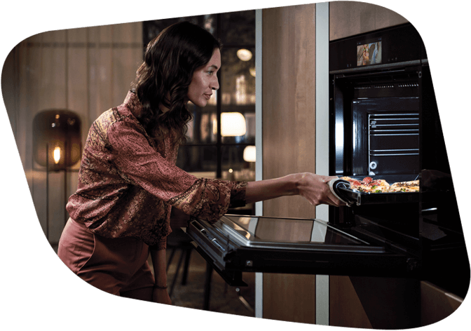 Frau schiebt ein Backblech mit leckerem Gericht in den neuen Siemens Backofen.