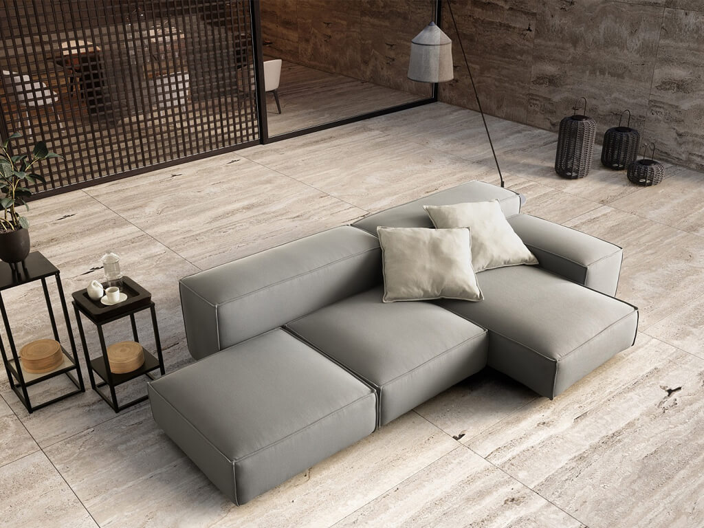 Eine Draufsicht auf ein modulares Outdoor-Sofa in Dunkelgrau mit hellbeigen Kissen, platziert auf einer hellen Steinfläche neben einem Pool. Im Hintergrund sind ein modernes Gebäude und ein Stehtisch mit einer Pflanze zu sehen.