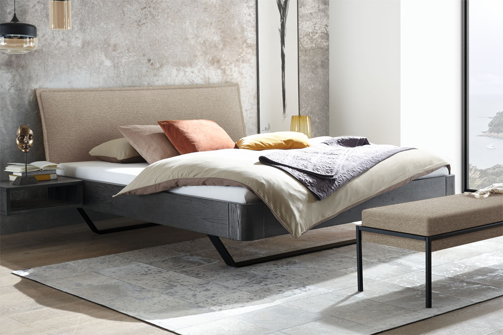 Modernes Bett mit schwarzem Rahmen und schwarzen Kufen und eine braunen Polsterkopfteil mit passender Bettbank auf Metallbeinen stilvoll dekoriert in einem modernen Zimmer