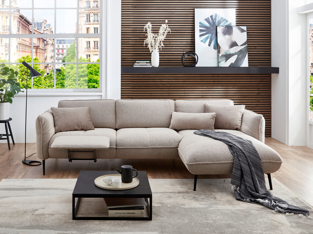 Poco Murcia - Polstergarnitur | Eckkombination | Space nature Ein modernes beiges Sofa vor einer Holzwand mit Dekoration, umgeben von einem Couchtisch und einer großen Fensterfront mit Blick auf eine Stadtansicht.