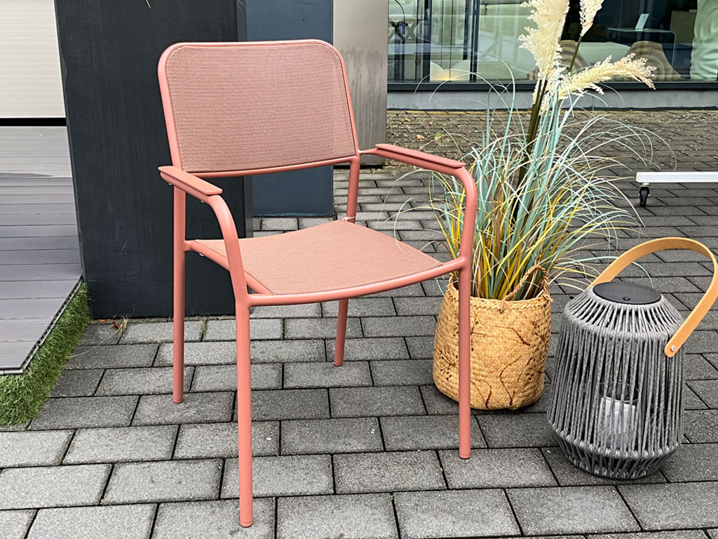 Korallfarbener Gartenstuhl mit Armlehnen, Netzbespannung an Sitz und Rückenlehne sowie schlankem Metallgestell.