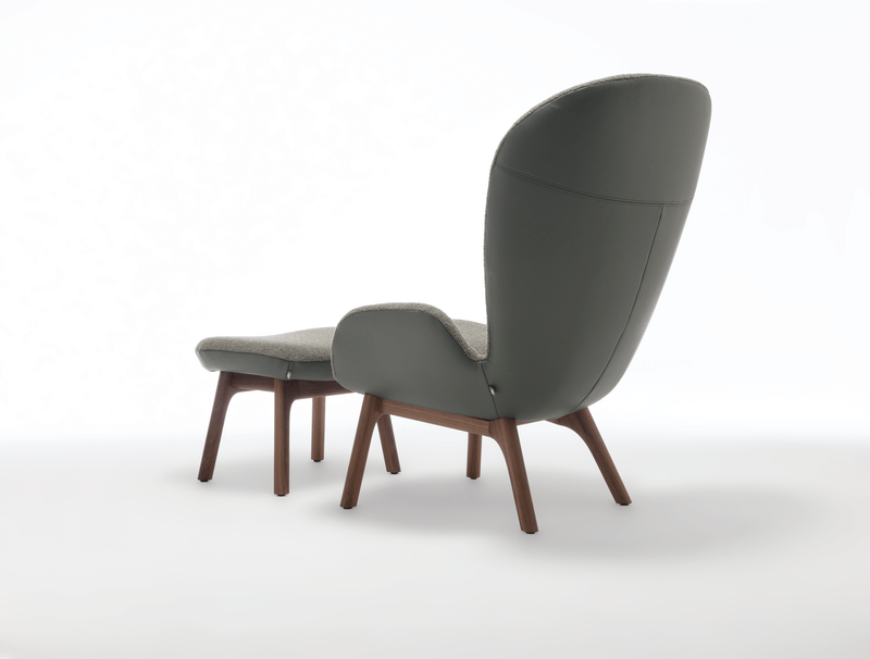 Rückansicht eines modernen Ohrensessels mit grauem Stoffbezug und einem passenden Fußhocker, beide mit Holzbeinen