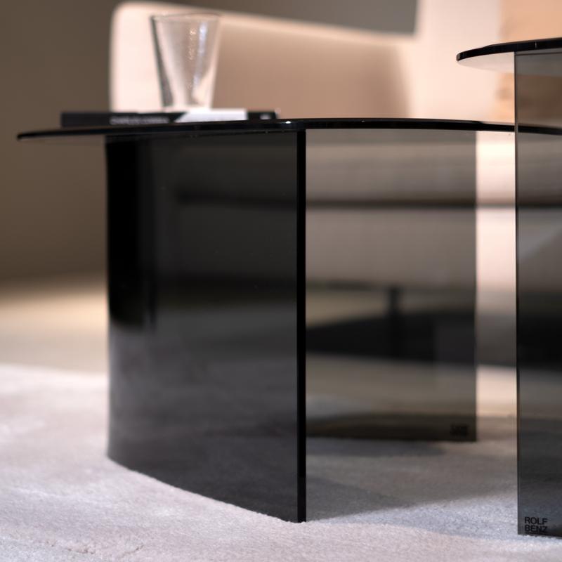 Nahaufnahme eines modernen Glastisches auf hellem Teppich, im Hintergrund ein Glas und ein Buch auf dem Tisch platziert