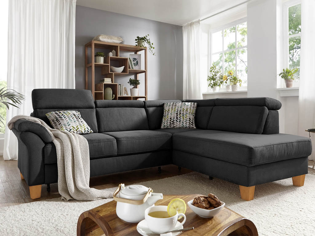 sit&more Santus | Polstergarnitur | 7281/7381 Dunkelgraues Ecksofa in einem hellen Wohnzimmer mit Kissen und Decke dekoriert