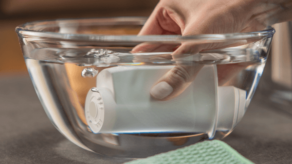 Eine Hand taucht den weißen Siemens BRITA Intenza Wasserfilter horizontal in eine Glasschüssel voller Wasser, um ihn vorzubereiten.