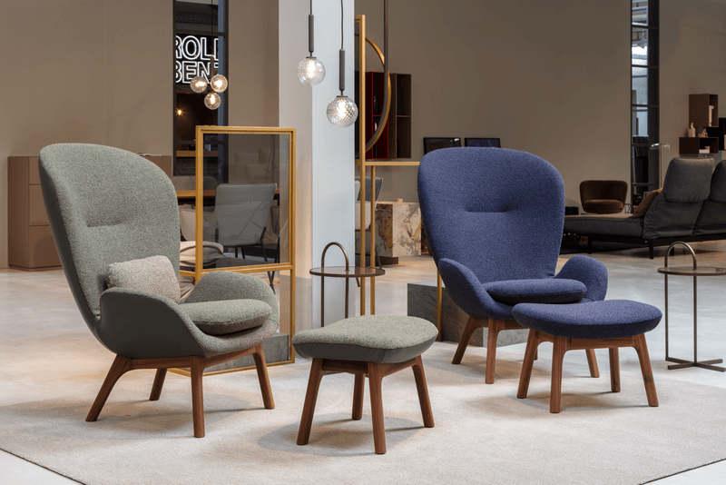 Zwei gemütliche Sessel mit Polsterung, ein grauer und ein blauer, mit passenden Hockern auf einem hellen Teppich in einem modernen Wohnzimmer.