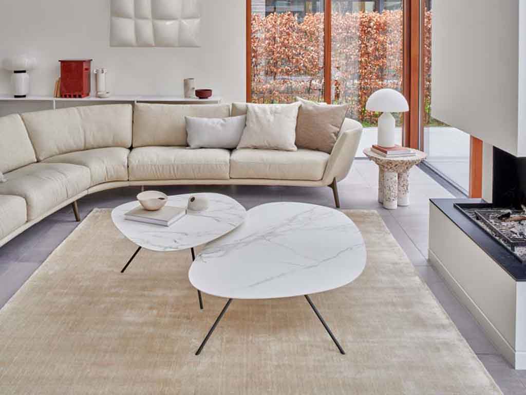 Helles Wohnzimmer mit beige Eckcouch, zwei Marmor-Couchtischen und großen Fenstern im Hintergrund