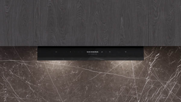 Nahaufnahme der Unterseite einer schwarzen Dunstabzugshaube, die elegant in eine dunkle Küchenzeile integriert ist. Das beleuchtete Bedienfeld befindet sich über einer dunkel marmorierten Arbeitsplatte.