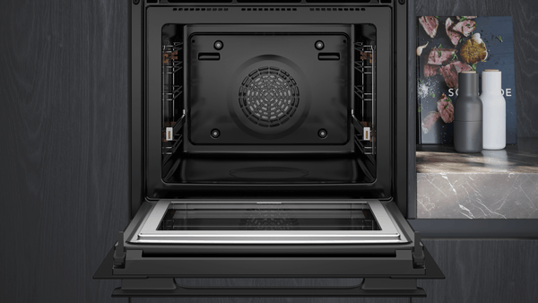 Blick in den leeren, emaillierten Innenraum des geöffneten Backofens mit Fokus auf das Rückwandgebläse und die seitlichen Einhängegitter.