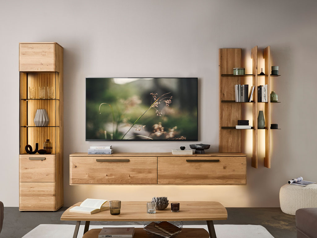 moderne Wohnwand aus Eiche mit einem beleuchtetem Hängelowboard, Aufsatzregal und Standvitrine stilvoll dekoriert in einem modernem Zimmer
