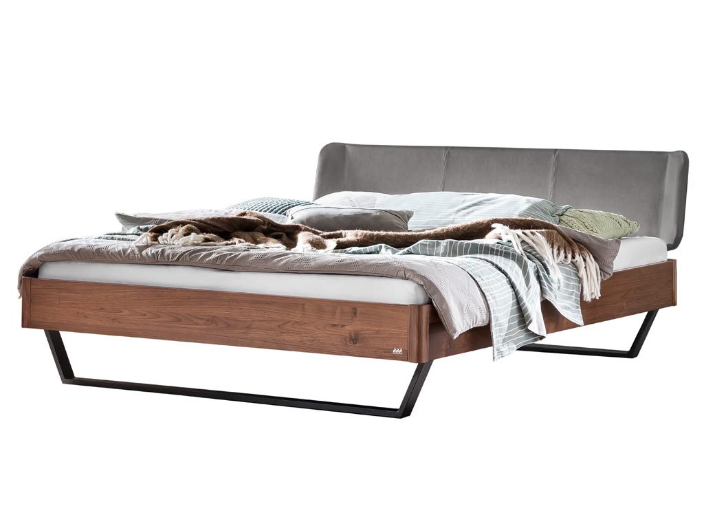 Ein hochwertiges Holzbett mit einem dunkelbraunen Rahmen aus Nussbaumholz. Das Bett hat ein hohes, gepolstertes Kopfteil in Anthrazit und steht auf einem modernen, schwarzen Metallgestell. Die Bettwäsche ist in hellen, natürlichen Tönen gehalten.
