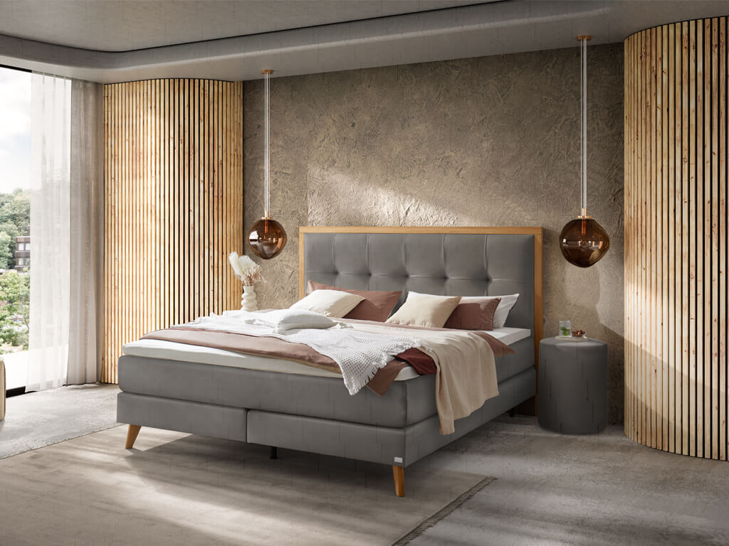 Ein modern eingerichtetes Schlafzimmer mit einem grauen Boxspringbett, einem strukturierten Kopfteil und Holz-Applikationen an der Wand.