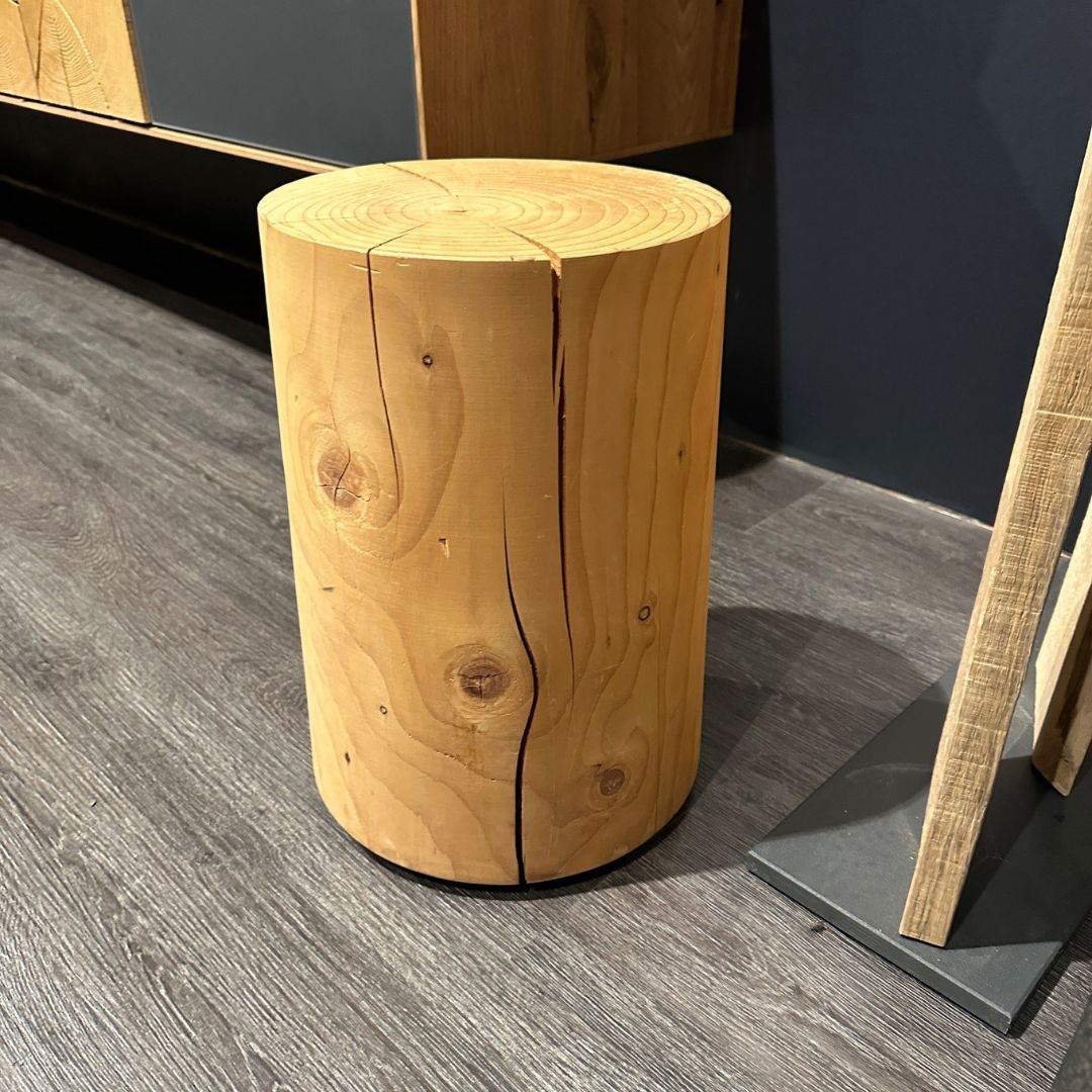 Ein massiver Holzhocker aus einem naturbelassenen Baumstamm auf einem dunklen Holzboden