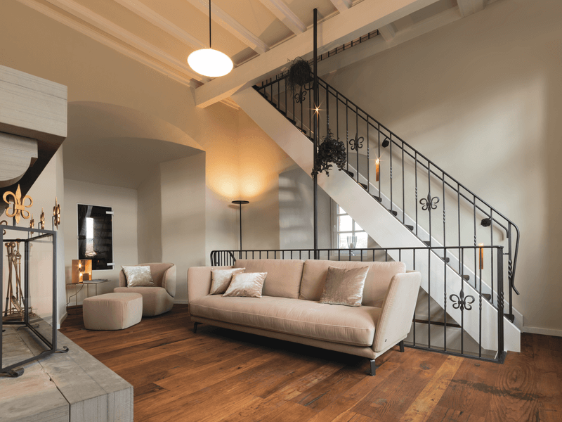 Wohnzimmer mit beigem Sofa, Treppe mit Metallgeländer und Holzfußboden