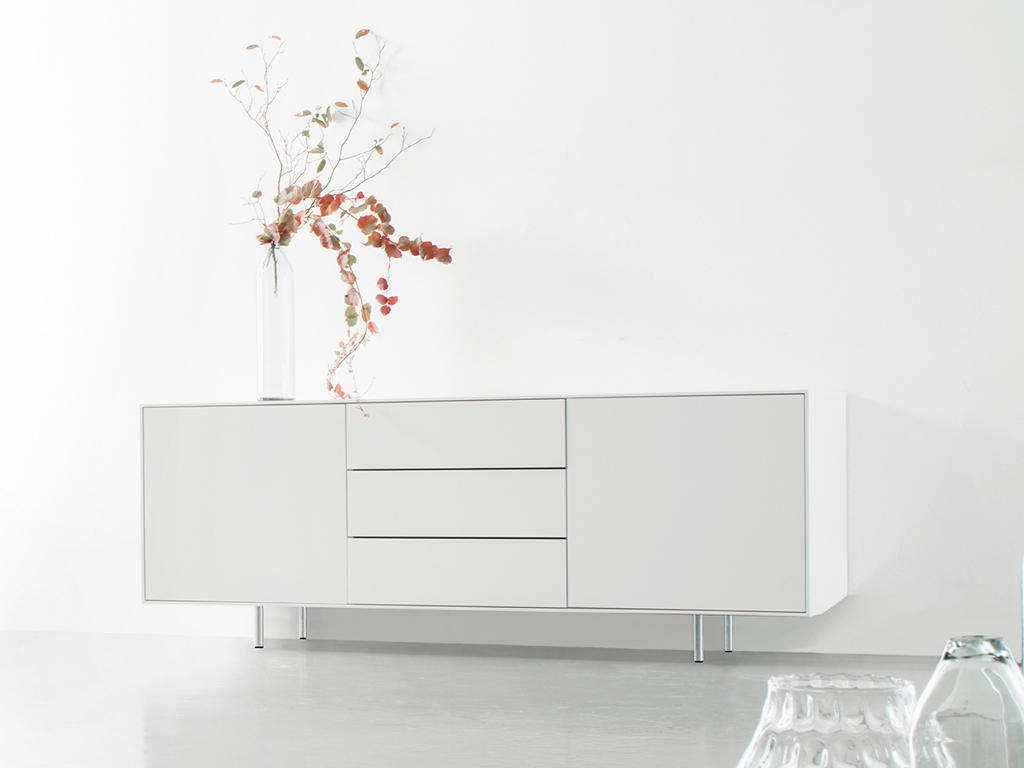 Sudbrock Game - Sideboard inkl. Chromfüße | Lack verkehrsweiß | B: 180 cm Ein modernes weißes Sideboard in einem minimalistischen Raum, dekoriert mit einer Glasvase und Zweigen