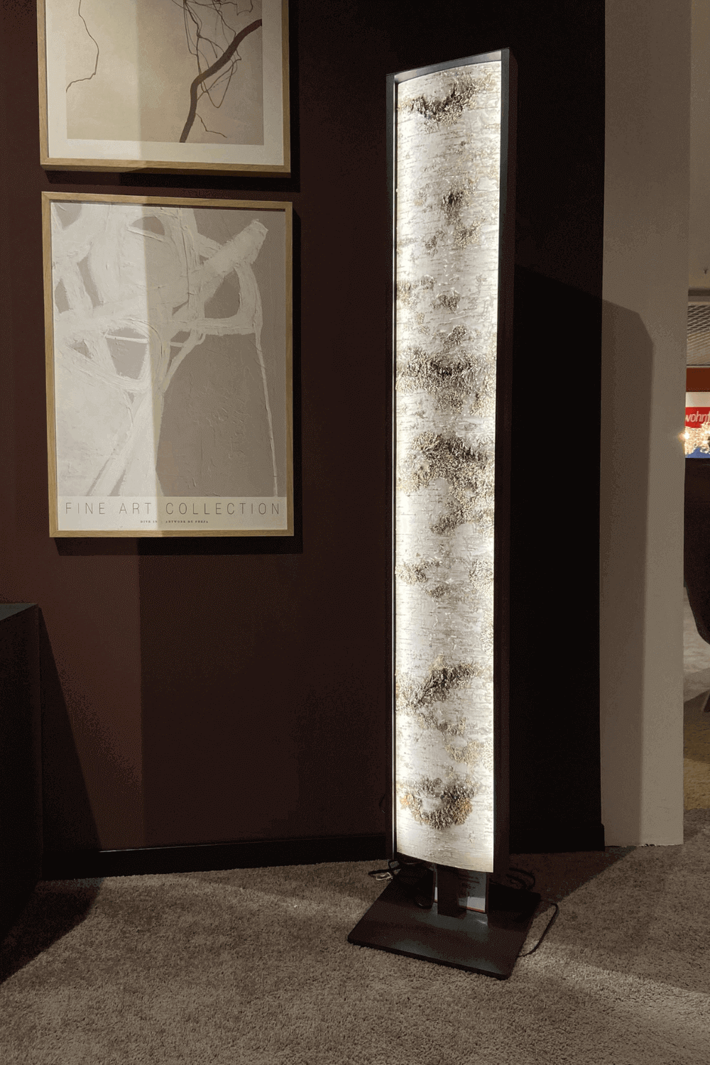 Eine stilvolle Stehlampe mit Holztextur an einer dunkelroten Wand, neben Wandkunst.