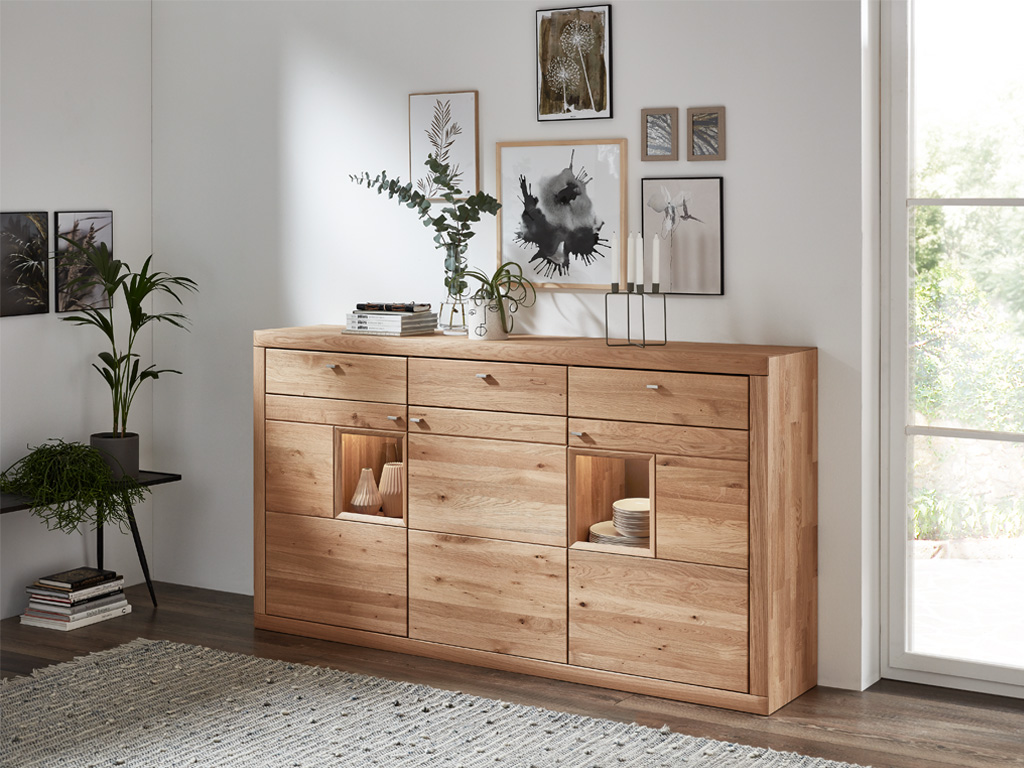 Wöstmann Aurum - Highboard | Type 2841 / 2041 | Wildeiche massiv | 2 Größen konfigurierbar Modernes Wohnzimmer mit elegantem Holz-Sideboard, dekoriert mit Pflanzen, Büchern und Bildern an der Wand