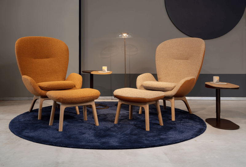 Zwei orangefarbene Designer-Sessel mit passender Ottomane auf einem blauen Teppich, flankiert von kleinen Holztischen und einer Stehlampe