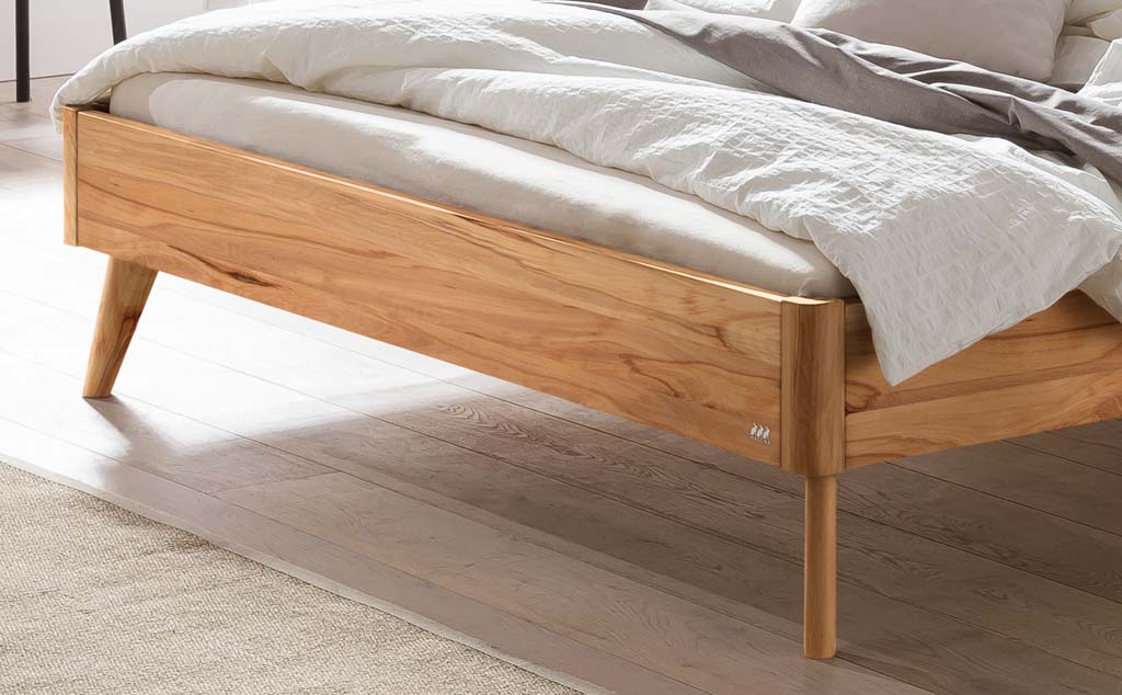 Detailaufnahme eines hellbraunen Holzbettes mit Holzfüßen in einem hellen Raum