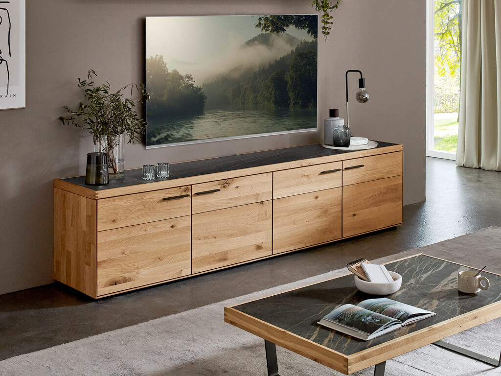 Langes TV-Lowboard aus Holz mit dunkler Deckplatte, ergänzt durch ein passendes Wandboard und eine hängende Glasvitrine.