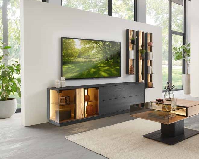 hartmann Kilva - Wohnwand | V22 | B: 296 cm Stylisches Wohnzimmer mit großem TV, modernem TV-Möbel und dekorativem Couchtisch in einem hellen, offenen Raum mit großen Fenstern.