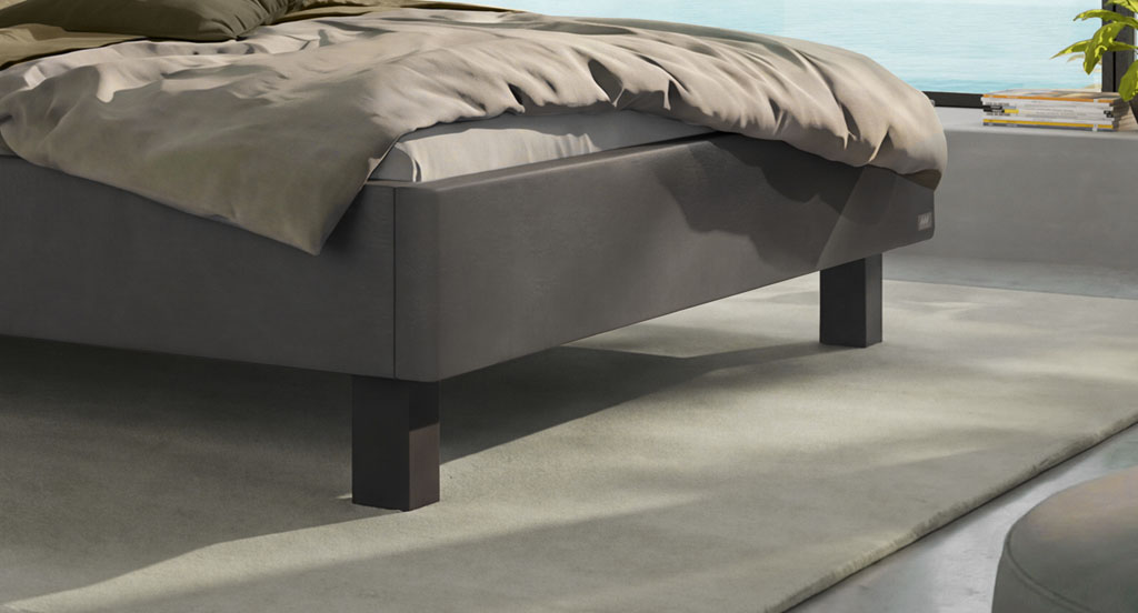 Nahaufnahme der massiven schwarzen Bettfüße am grauen Polsterbett in einem modernen Schlafzimmer am See (KI-generiert)