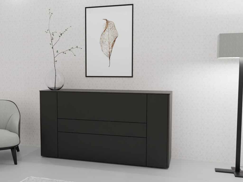 Sudbrock Goya - Sideboard | 2 Türen, 2 Schubladen, 1 Klappe | B: 175,2 cm | Lack cosmos-schwarz Ein modernes schwarzes Sideboard mit minimalistischem Design, dekoriert mit einem Glas mit Zweigen. Daneben ein gemütlicher Sessel und eine Stehlampe, an der Wand ein Bild mit Blattmotiv.