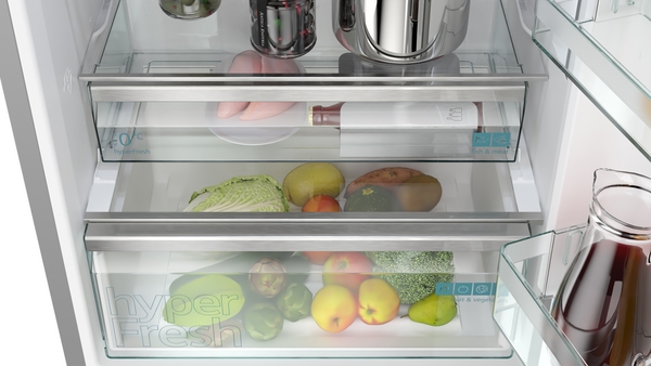Innenansicht eines modernen Kühlschranks mit hyperFresh-Schubladen, die Obst und Gemüse frisch halten. Enthält verschiedene Lebensmittel und eine Wasserflasche.